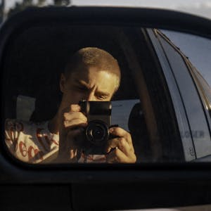 A photographer captures a self-portrait using a car's side mirror at golden hour.